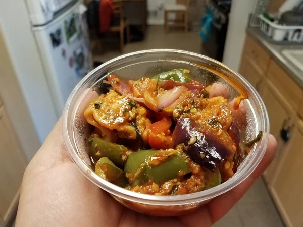 Hand holding plastic container of spicy meat with peppers in kitchen — 스톡 사진