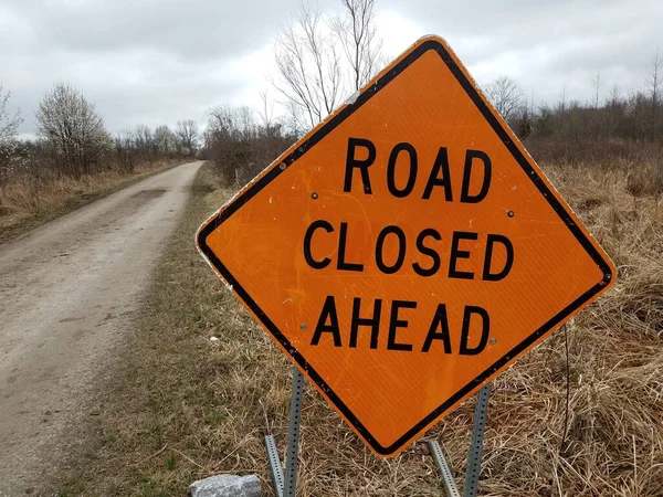 orange road closed ahead sign with trail or path