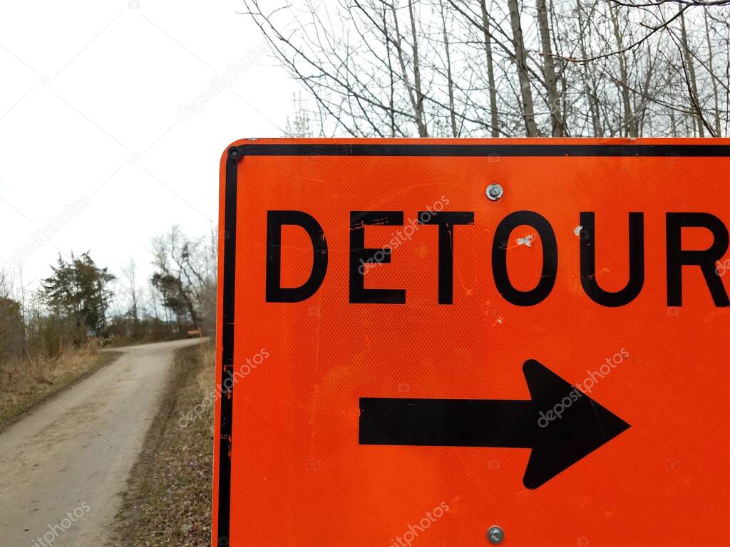 orange detour sign with black arrow with trail or path