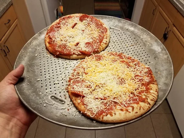 Mão segurando bandeja de cozimento de metal com pizzas — Fotografia de Stock