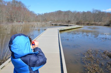 Mavi ceketli çocuk sulak alanda dürbün kullanıyor.