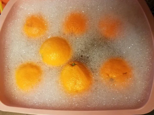 Апельсины в мыльной воде в розовой пластиковой ванне — стоковое фото