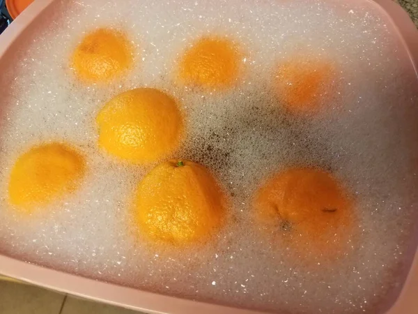 Oranges dans de l'eau savonneuse dans une baignoire en plastique rose — Photo