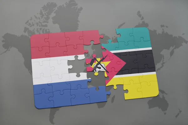Rompecabezas con la bandera nacional de los Países Bajos y Mozambique en un mapa del mundo de fondo . — Foto de Stock