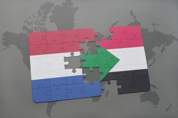 Quebra-cabeça com a bandeira nacional das terras baixas e sudan em um fundo de mapa do mundo . — Fotografia de Stock