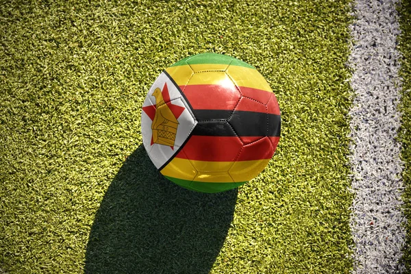 Bola de futebol com a bandeira nacional de zimbabwe encontra-se no campo — Fotografia de Stock