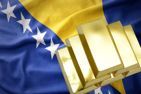 Luccicanti lingotti d'oro sulla bandiera bosniaca ed erbosa — Foto Stock