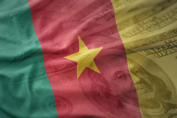 Colorido ondeando bandera nacional de camerún sobre un fondo de dinero en dólares americanos . — Foto de Stock