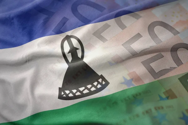 Coloré agitant le drapeau national du lesotho sur un fond de billets en euros. concept de financement — Photo