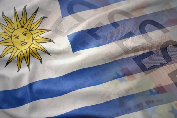 Colorido ondeando bandera nacional de uruguay sobre un fondo de billetes de dinero en euros. concepto de financiación —  Fotos de Stock
