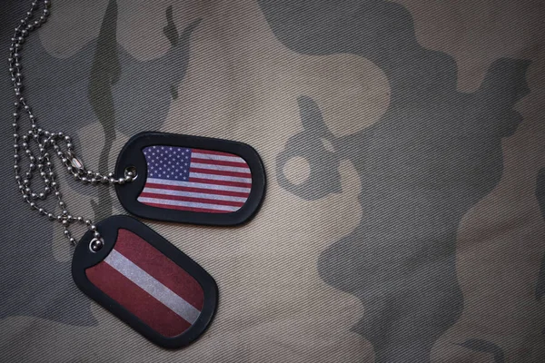 Армія пуста, собача мітка з прапором об'єднаних держав америки і латвії на тлі текстури хакі. військова концепція — стокове фото