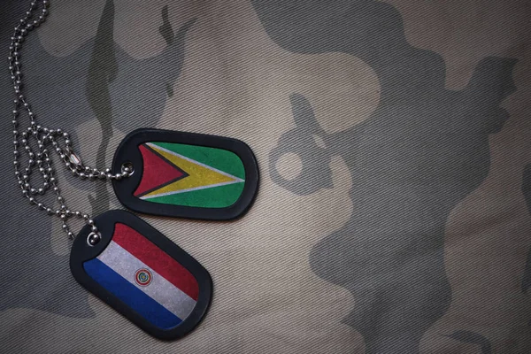 Army blank, dog tag with flag of guyana and paraguay on the khaki texture background. military concept — Stock Photo, Image