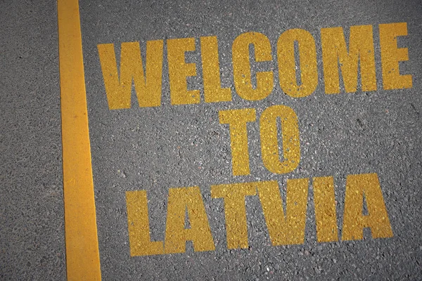 Асфальтована дорога з текстом ласкаво просимо до Латвії біля жовтої лінії . — стокове фото