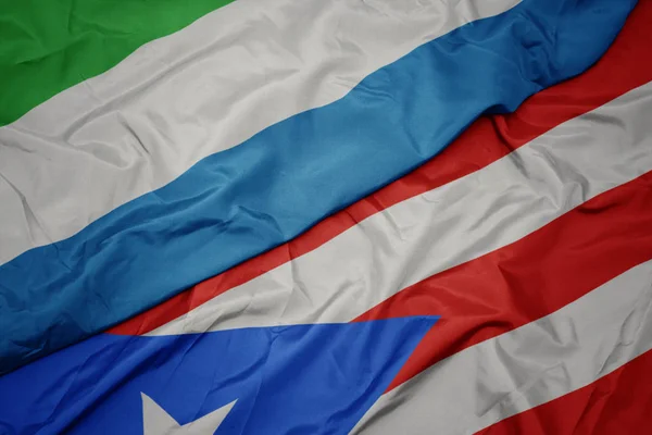 Ondeando colorida bandera de Puerto Rico y bandera nacional de Sierra Leona . — Foto de Stock