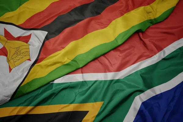 Acenando bandeira colorida da África do Sul e bandeira nacional de zimbabwe . — Fotografia de Stock