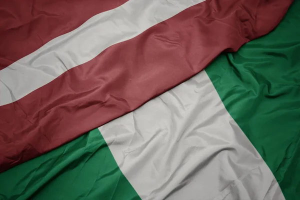 Waving colorful flag of nigeria and national flag of latvia. — Stock Photo, Image