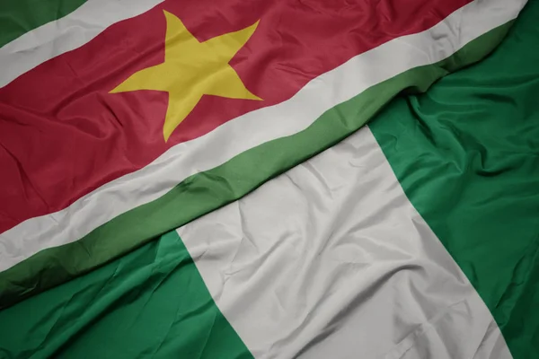 Ondeando colorida bandera de nigeria y bandera nacional de surinam . — Foto de Stock