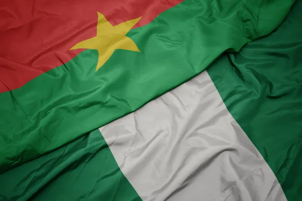 Ondeando colorida bandera de nigeria y bandera nacional de burkina faso . — Foto de Stock