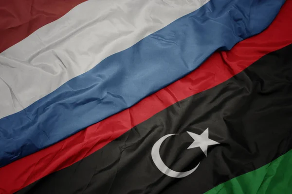 Ondeando colorida bandera de libya y bandera nacional de luxembourg . — Foto de Stock