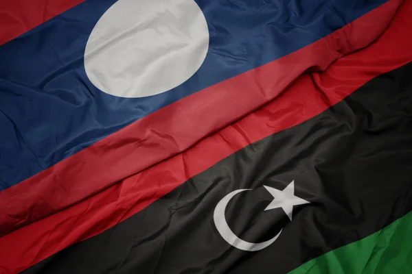 Ondeando colorida bandera de libya y bandera nacional de laos . — Foto de Stock