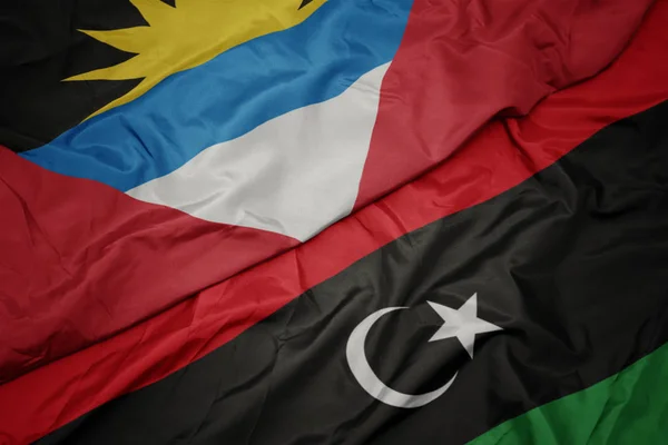 Ondeando colorida bandera de libya y bandera nacional de antigua y barbuda . — Foto de Stock