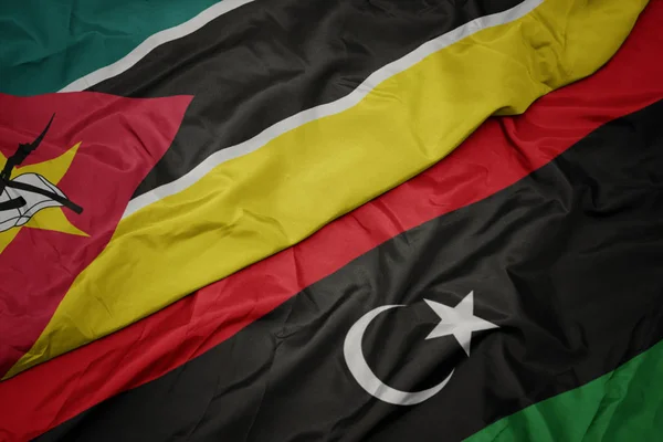 waving colorful flag of libya and national flag of mozambique.