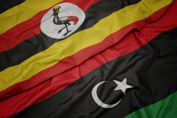 Líbia színes lobogója és ugandai nemzeti zászló lobogtatása. — Stock Fotó