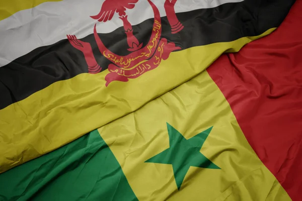 Ondeando colorida bandera de senegal y bandera nacional de brunei . — Foto de Stock
