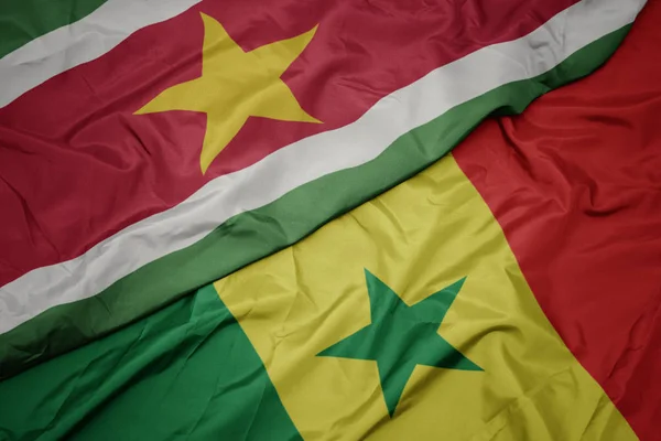 Ondeando colorida bandera de senegal y bandera nacional de surinam . — Foto de Stock