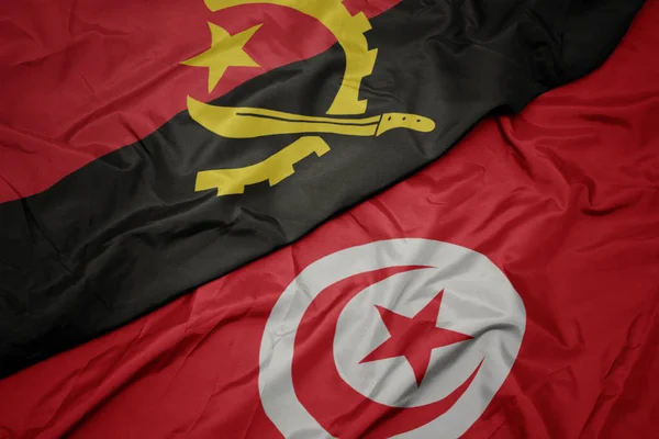 Waving colorful flag of tunisia and national flag of angola. — Stock Photo, Image