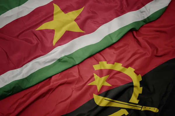 Ondeando colorida bandera de angola y bandera nacional de surinam . — Foto de Stock