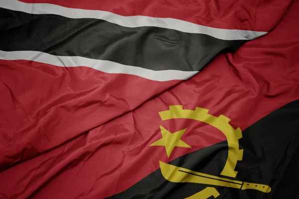 Ondeando colorida bandera de angola y bandera nacional de trinidad y tobago . — Foto de Stock