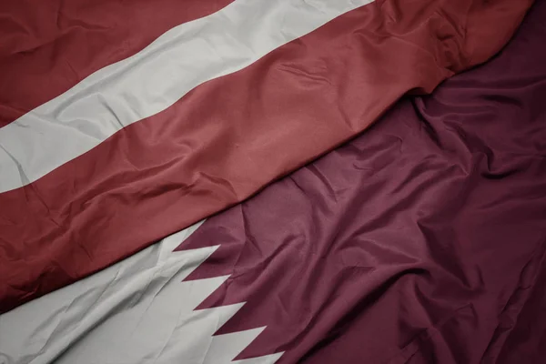 Falująca kolorowa flaga Kataru i flaga narodowa Łotwy. — Zdjęcie stockowe