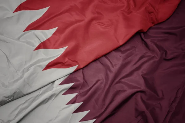 waving colorful flag of qatar and national flag of bahrain.