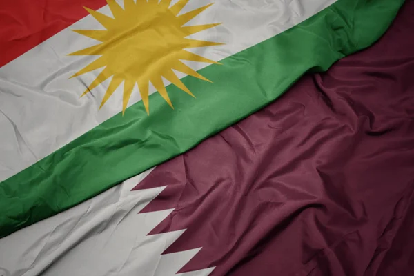 Zwaaiende kleurrijke vlag van Qatar en nationale vlag van Kurdistan. — Stockfoto