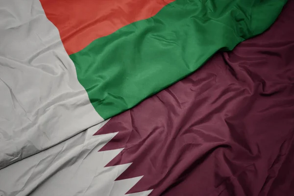 Viftande färgglada flagga qatar och nationell flagga madagascar. — Stockfoto