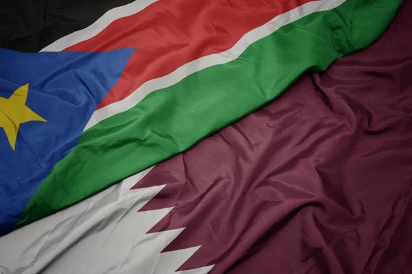 Ondeando colorida bandera de qatar y bandera nacional de sudan del sur . —  Fotos de Stock