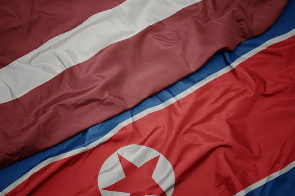 Falująca kolorowa flaga Korei Północnej i flaga narodowa Łotwy. — Zdjęcie stockowe