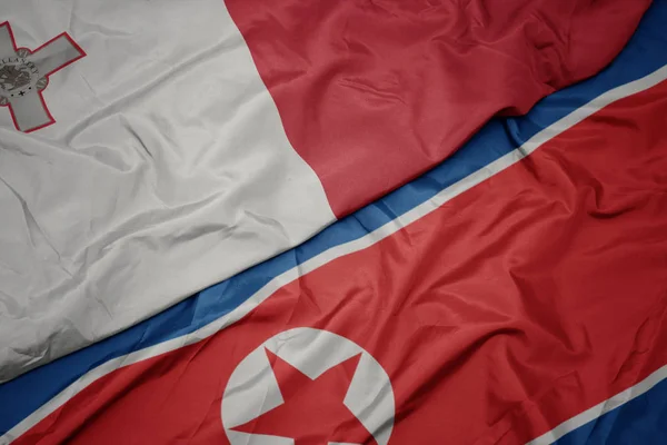Schwenken bunte Flagge Nordkoreas und Nationalflagge Maltas. — Stockfoto