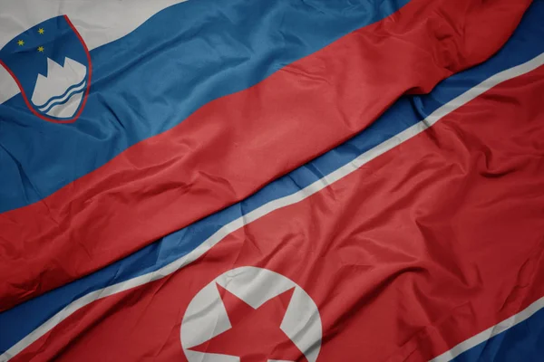 Mávání barevnou vlajkou Severní Koreje a národní vlajkou Slovinska. — Stock fotografie