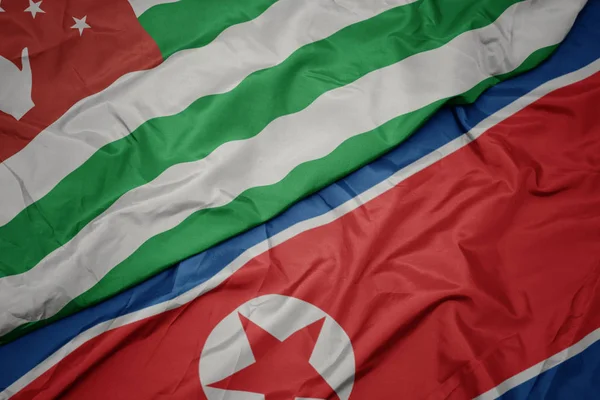 Ondeando colorida bandera de Corea del Norte y bandera nacional de abjasia . — Foto de Stock