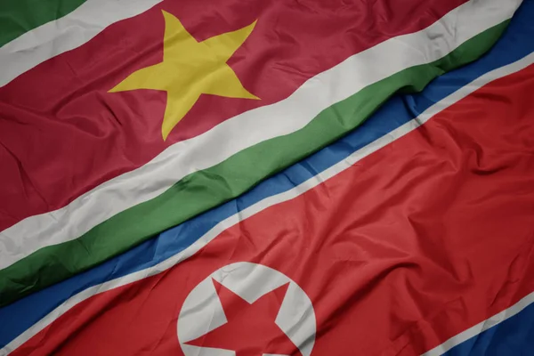 Ondeando colorida bandera de Corea del Norte y bandera nacional de surinam . — Foto de Stock