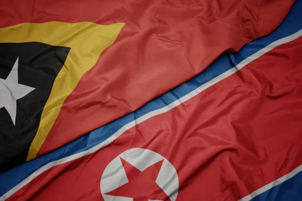 Ondeando colorida bandera de Corea del Norte y bandera nacional de Timor Oriental . — Foto de Stock