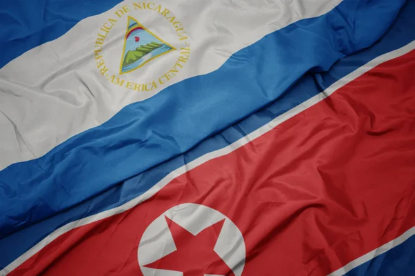 Machająca kolorowa flaga Korei Północnej i flaga narodowa Nikaragui. — Zdjęcie stockowe