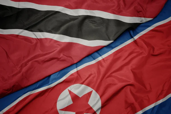 Ondeando colorida bandera de Corea del Norte y bandera nacional de trinidad y tobago . — Foto de Stock