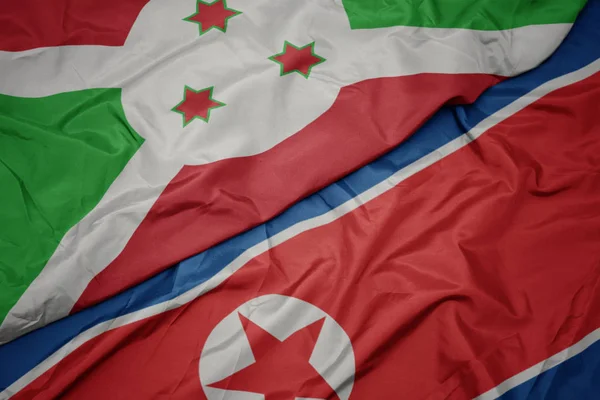 Ondeando colorida bandera de Corea del Norte y bandera nacional de Burundi  . — Foto de Stock