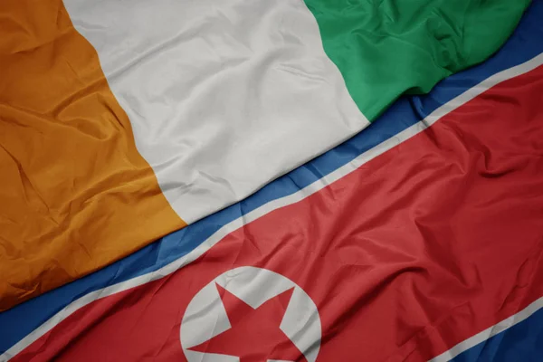 Machająca kolorowa flaga Korei Północnej i flaga narodowa Wybrzeża Kości Słoniowej. — Zdjęcie stockowe