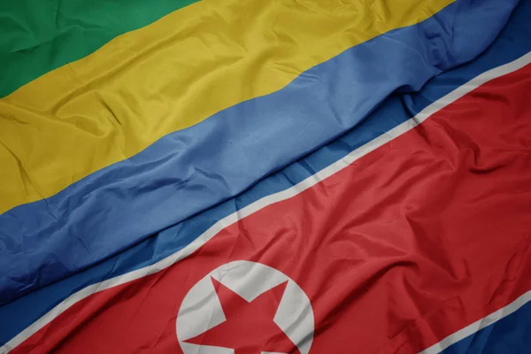 Ondeando colorida bandera de Corea del Norte y bandera nacional de Gabón . — Foto de Stock