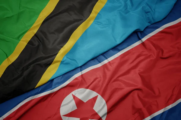 Ondeando colorida bandera de Corea del Norte y bandera nacional de tanzania . — Foto de Stock