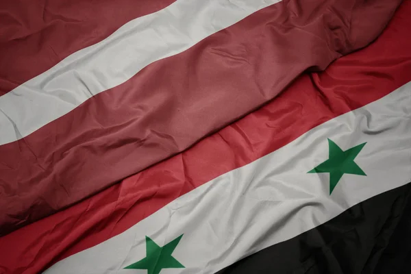 Zwaaiende vlag van syrië en nationale vlag van latvia. — Stockfoto
